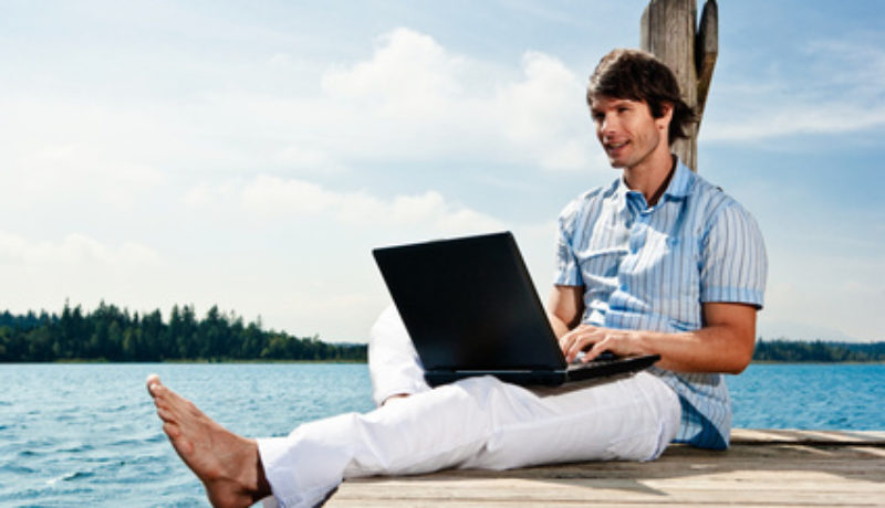 Mężczyzna pracuje przy komputerze, będąc nad jeziorem.