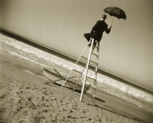 Ratownik morski siedzi na specjalnym krześle i trzyma otwarty parasol