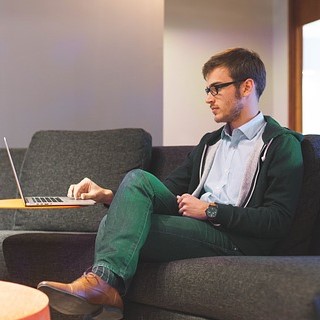 Man working on computer sitting on couch.